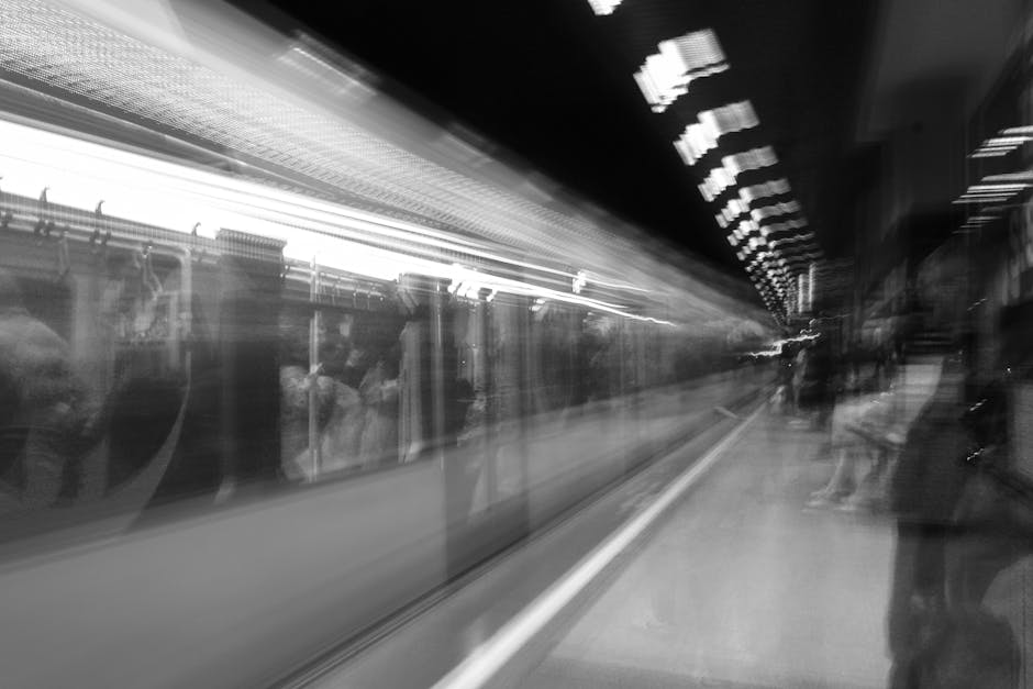People standing on a platform at Crayford Station in the UK, waiting to board a fast-moving train visible with blurred motion effects reflecting passengers inside. The scene shows a mix of adults and children, some carrying shopping bags and backpacks, positioned near the platform's edge with tactile paving and safety markings. The station's green and metal ceiling panels, along with the illuminated signage and doors of the train, are visible in the background. This setting illustrates the typical environment for a home relocation preparation or a commuter transfer, emphasizing efficient, timely transport processes associated with professional removals services such as those offered by Man with Van Crayford, particularly relevant for moving logistics and furniture transport related to house moves near Crayford station.