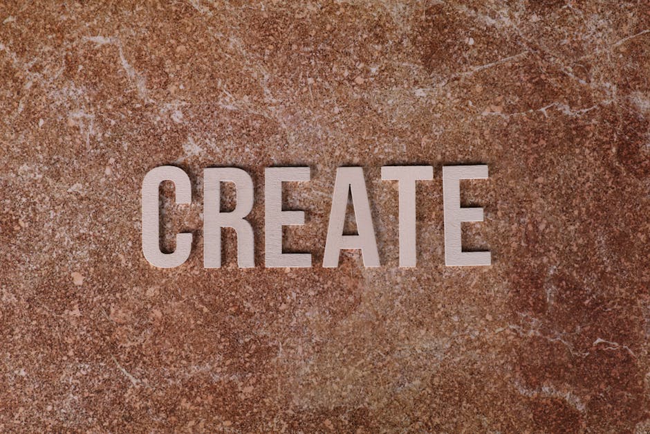 Close-up image of the word 'CREATE' displayed in three-dimensional white letters mounted on a textured, reddish-brown stone or brick wall. The lighting highlights the shadows cast by the letters, emphasizing their depth. The background surface has a rough, uneven finish typical of natural stone or brickwork, which may be part of a building interior or exterior setting. This visual could represent a motivational or inspirational sign in a home or business environment related to home relocation or moving services, such as those offered by Man with Van Crayford, whose website provides professional removals. The focus on the word 'CREATE' aligns conceptually with packing, planning, and organizing during a house move, especially in the context of furniture transport and moving logistics.